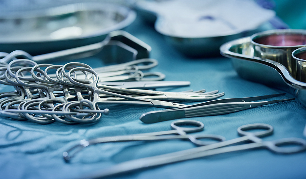 Imagem de pinças e instrumentos médicos metálicos sobre mesa cirúrgica.