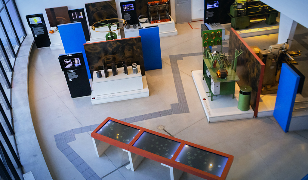 Vista aérea de sala de museu com equipamentos expostos em plataformas e painéis informativos.